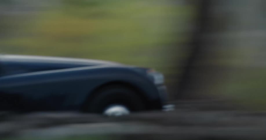 A car is driving fast down a road at dusk