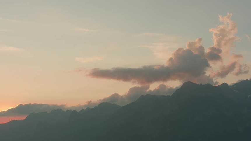 Sunset tints the sky and clouds red over a mountain range