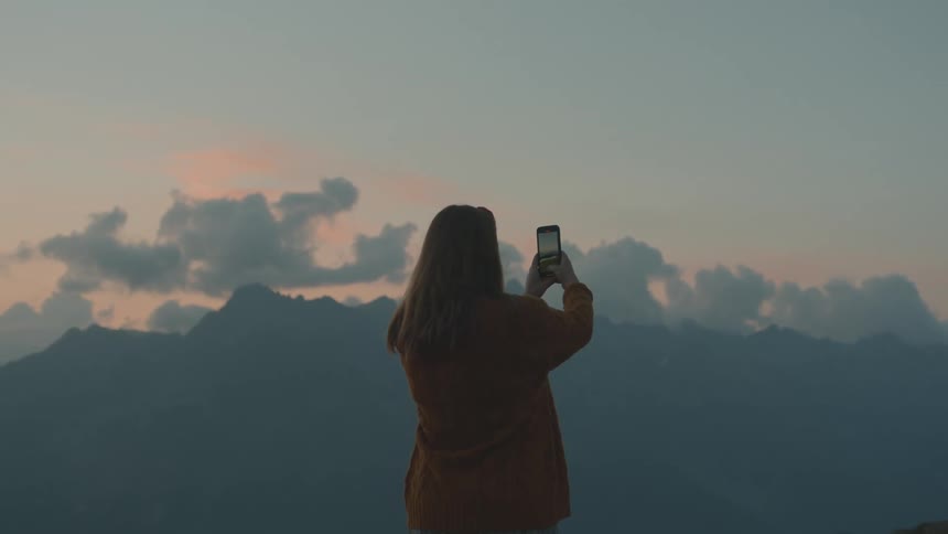 A woman stands outdoors taking a picture of the mountain view