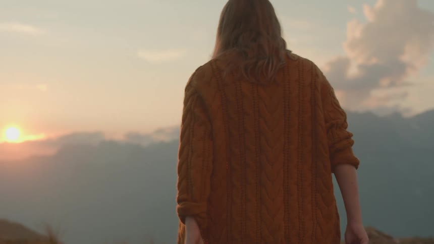 A woman in a yellow sweater hiking in mountains in early morning
