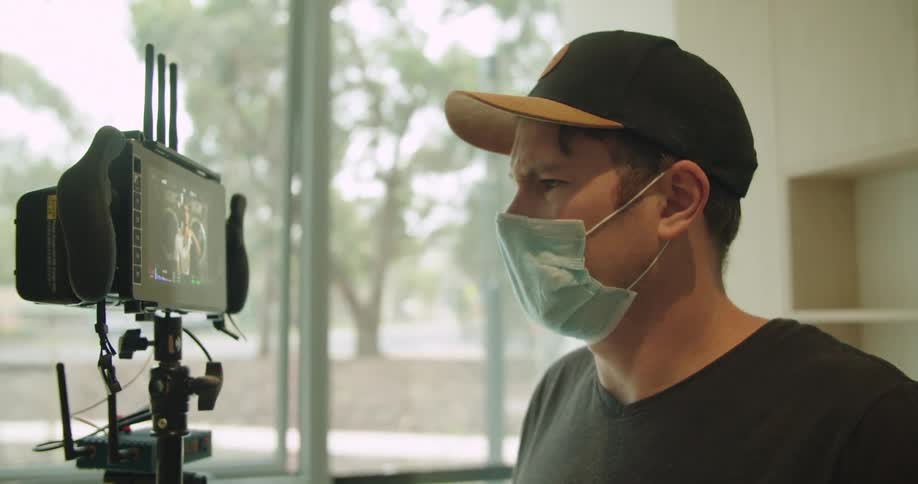 A man wearing a face mask looking at the footage recorded on a camera