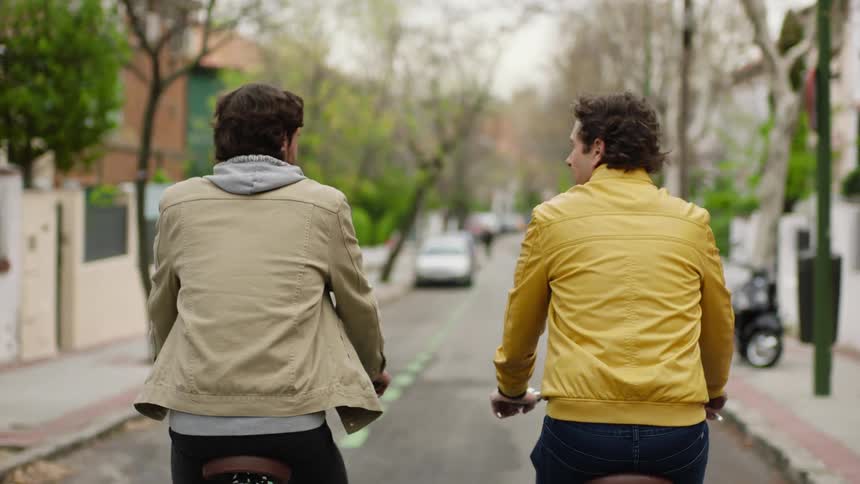 Two men are riding bikes down a street in spring