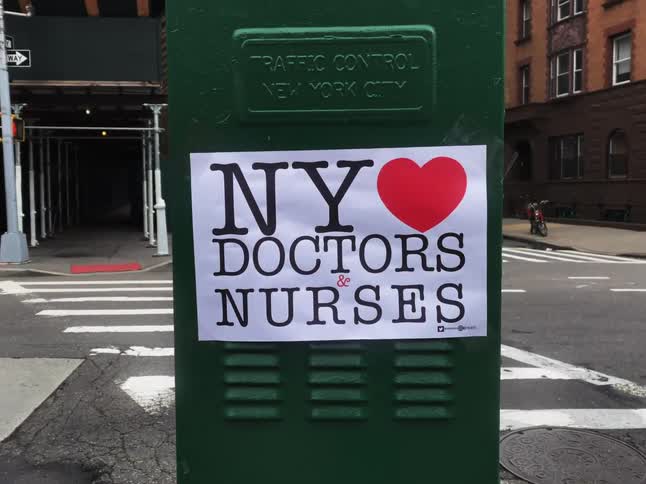 A sign for medical staff appreciation is on a green traffic control box on a street corner