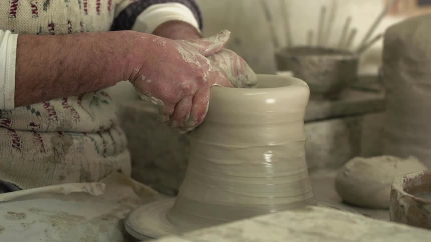 A man dips his fingers in water and rubs it on the clay as he molds pottery