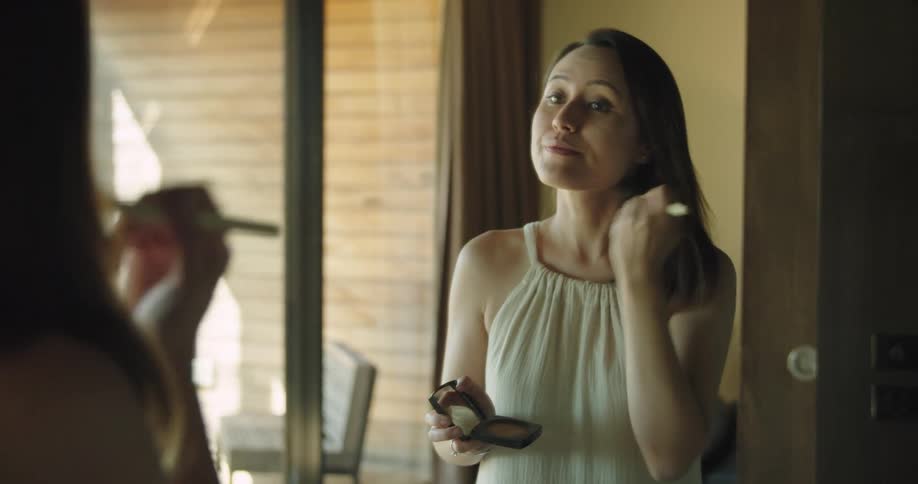 Woman applying makeup with a brush in front of a mirror at home
