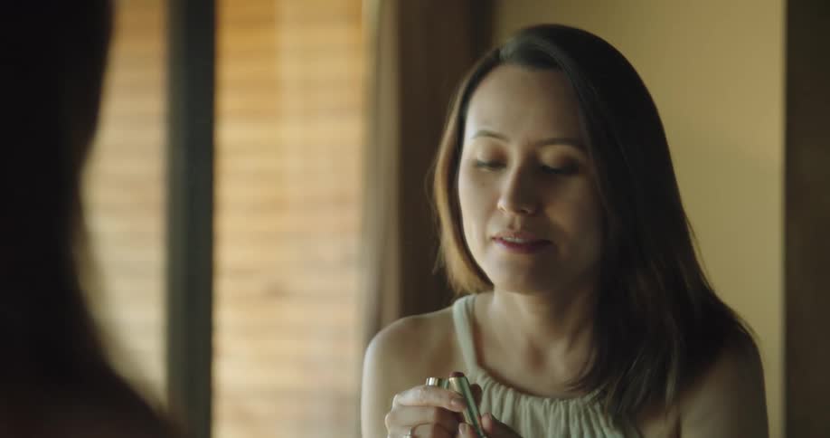A woman in a room looking into a mirror and putting on lipstick