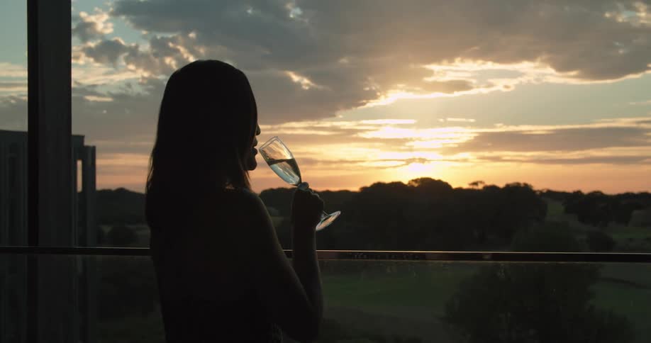A woman is standing outdoors and drinking alcohol at dusk