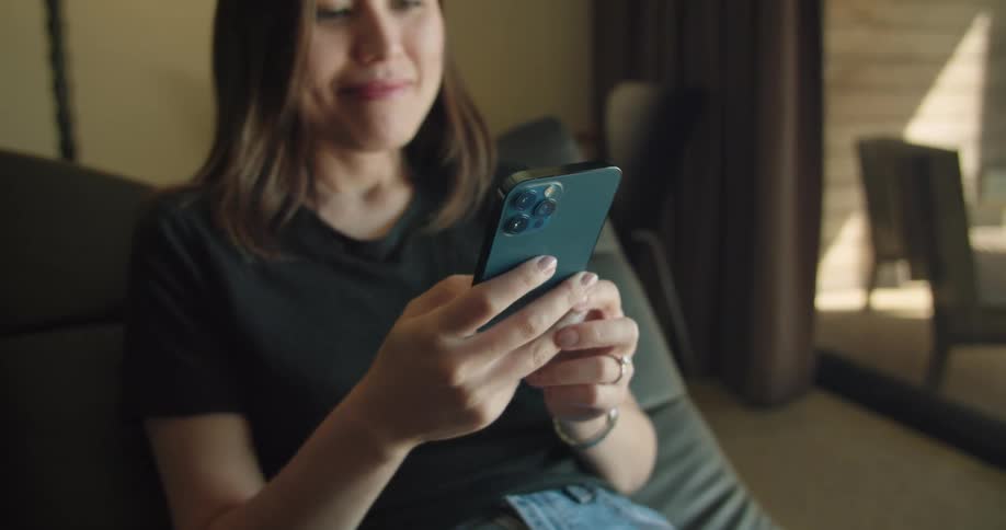 A woman is sitting down at home using her cell phone