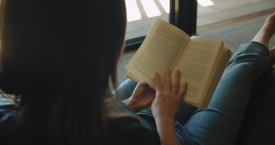 A woman is sitting on a chair and reading a book indoors