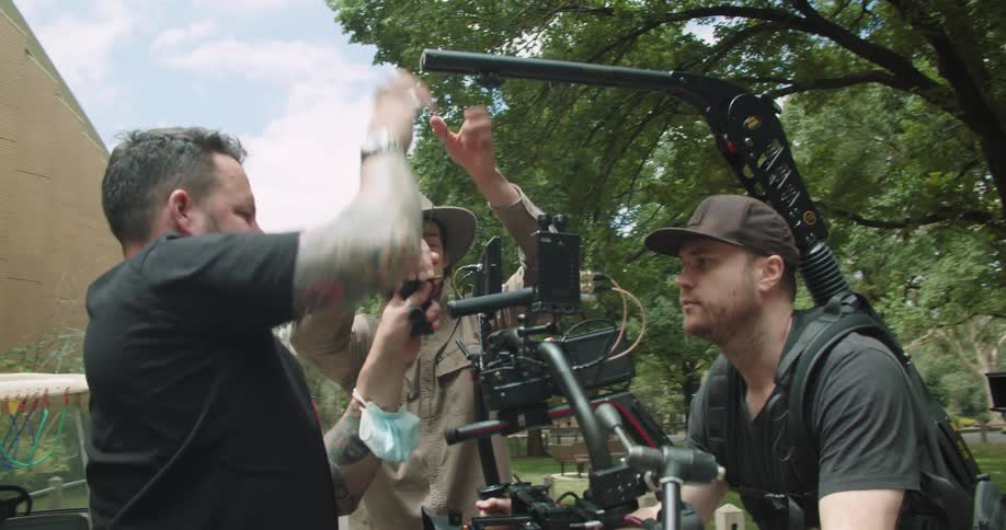 Film crew adjusting a camera righ on the shoulders of a camera man in a park