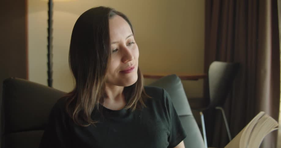 A woman is reading a book while sitting indoors
