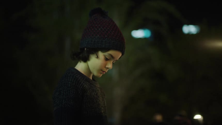 A young boy with his head lowered to the ground outside at night