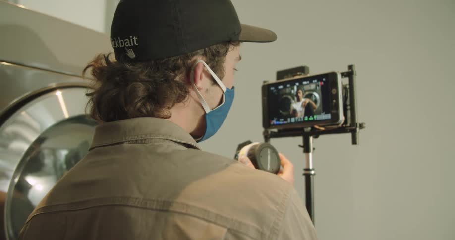 Camera operator wearing a face mask reviews footage on a screen over a tripod