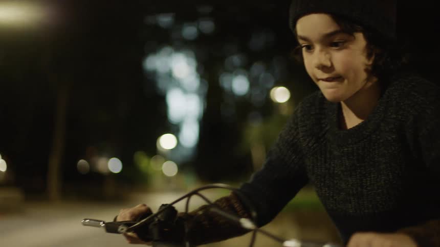 Person with beanie and grey pullover rides bicycle at night