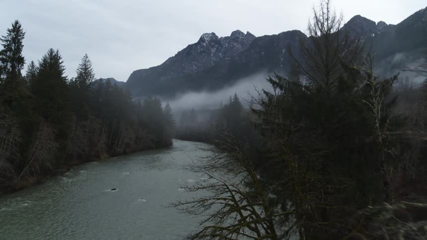 Ascent toward a river surrounded by misty trees and a rugged mountain range