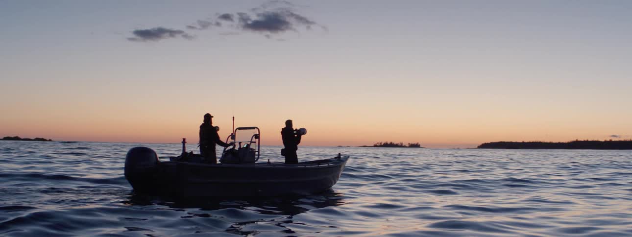 Two people on a boat in the middle of a body of water at dawn