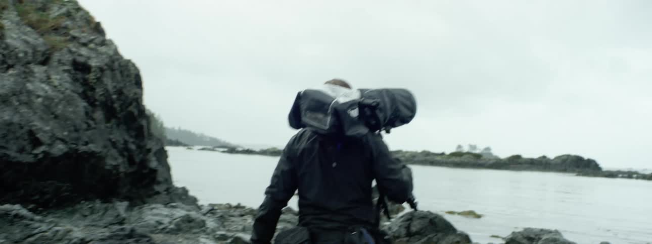 A person carries a camera along a coastline