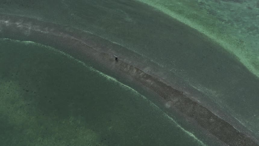 An aerial view of a person walking along the shore