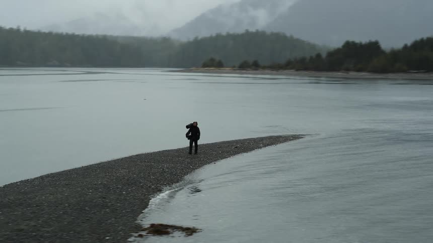 A man walks on a sand bar carrying equipment at dusk