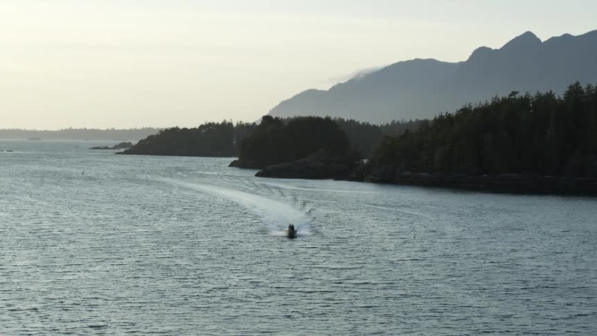 A motor boat leaves a wake as it travels near tree covered coast