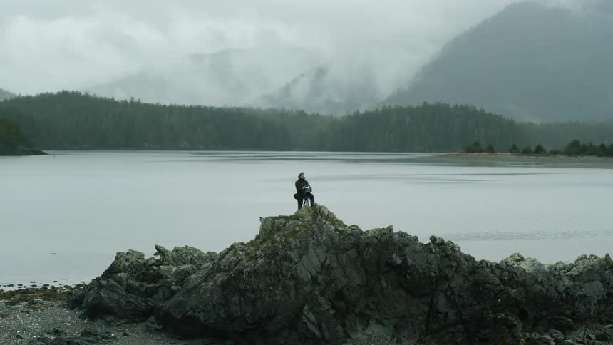 A photographer takes pictures from a cliff on the shore