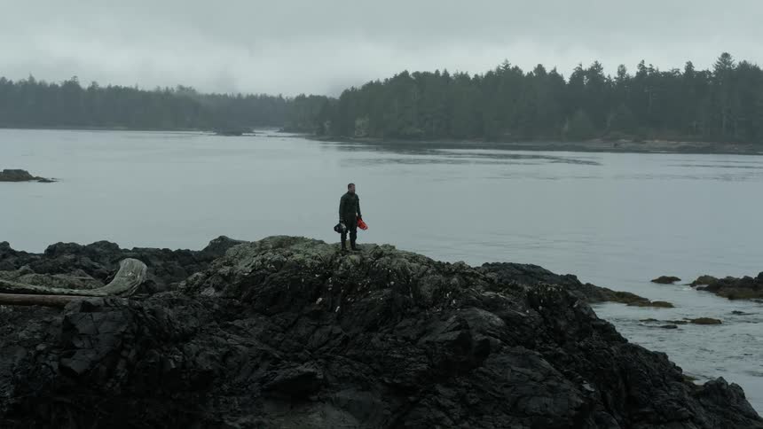 A man stands on a large rock on a coastline