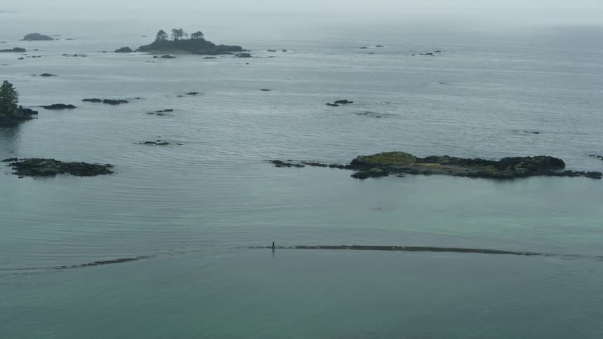 Landscape with ocean coastline and an island as well as a person walking in low tide on a sand bar
