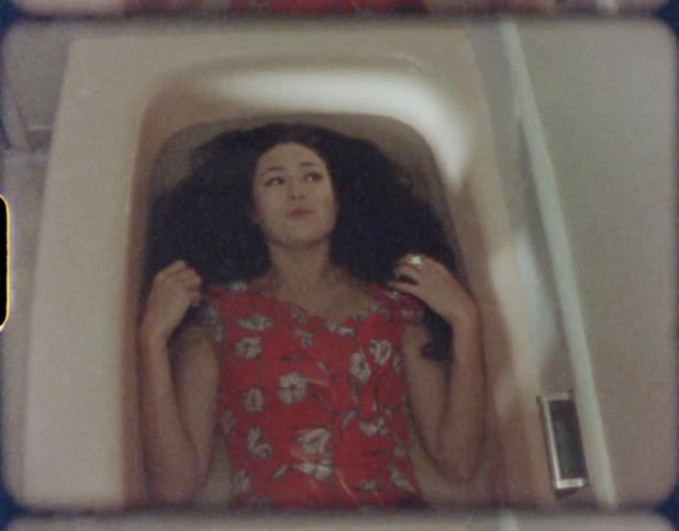 A woman lies in a bathtub while her body is submerged in water for a moment before slowly sitting up