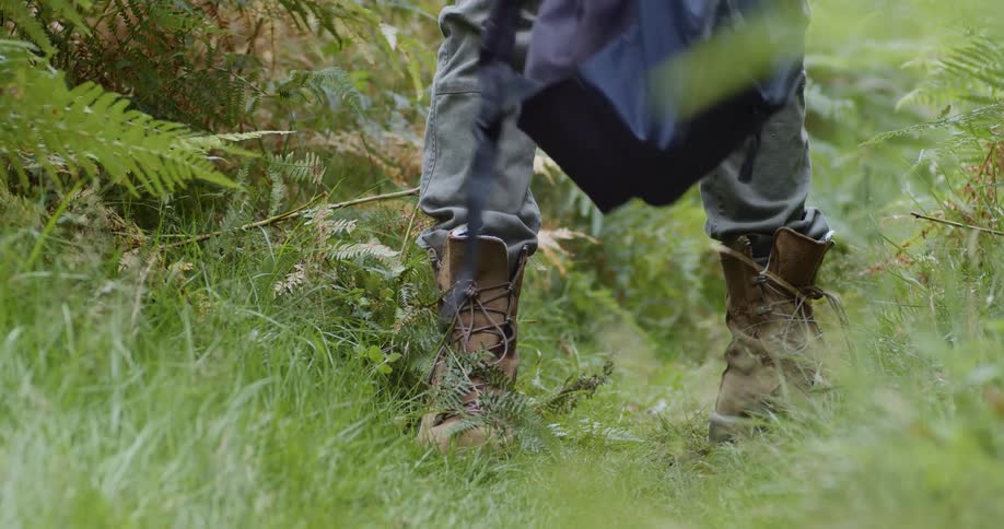 Man wearing boots stops in a trail on the forest to check his backpack