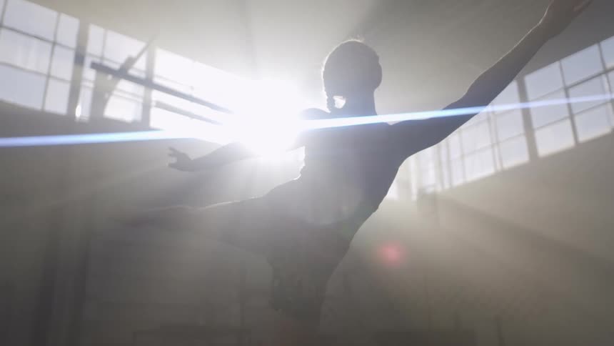 A woman completes ballet moves while inside a gym with light beams