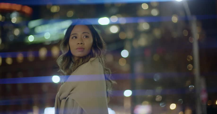 A young woman stands outside a building with the city lights lit up
