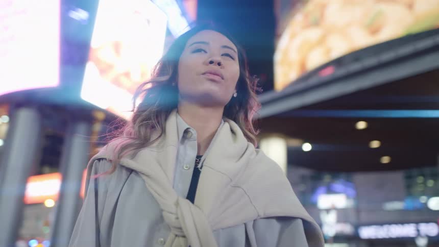 A young woman walks through a brightly lit metropolis at night