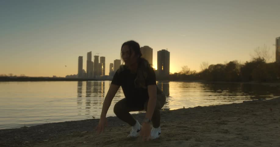 A woman works out in the sand going from push up to squat thrust and jumping up in the air