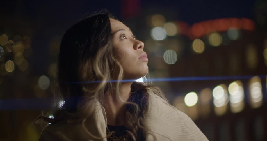 A woman looks up at bright city lights in downtown buildings