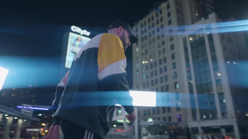 A man walks on a street in a downtown area with buildings digital displays and signs at night
