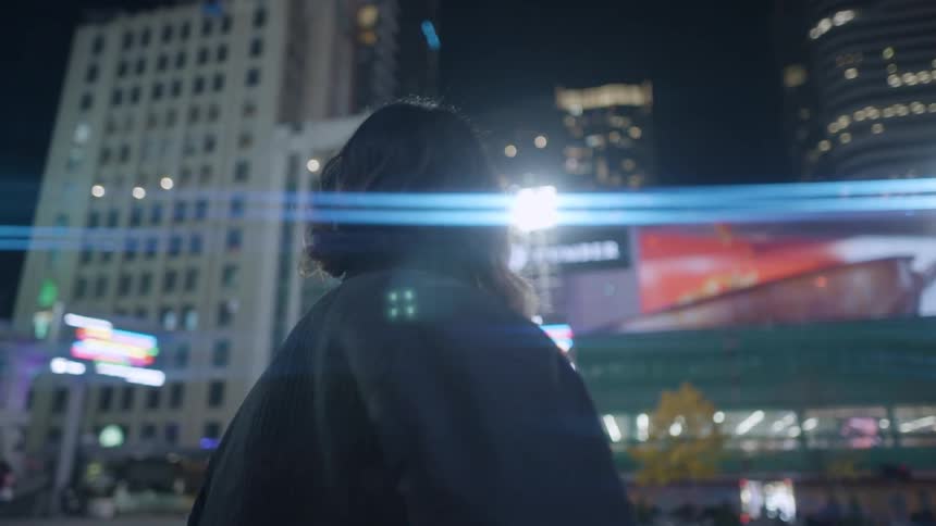 A woman looks up and watches a video playing on a billboard in front tall skyscrapers downtown