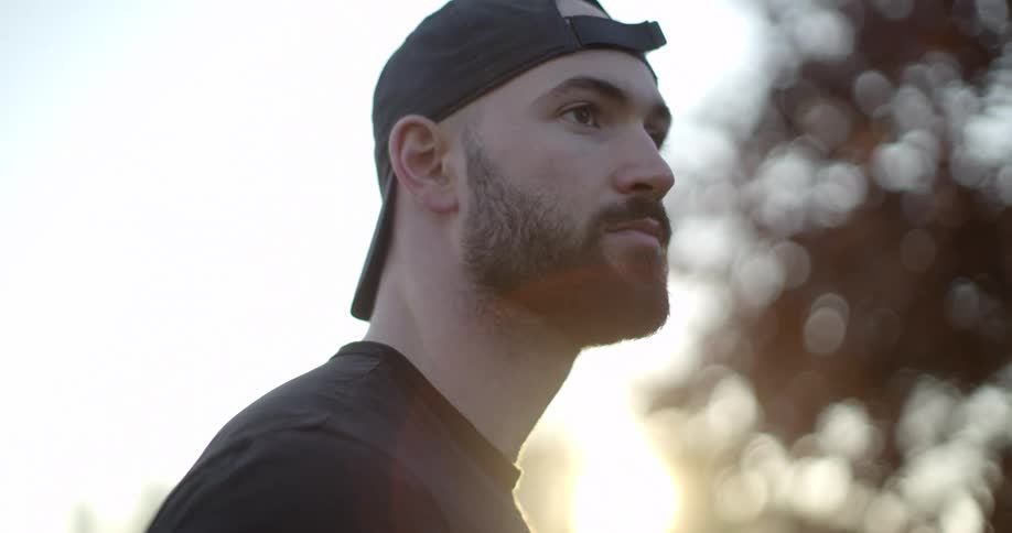 A man with a beard wearing a backwards hat outside