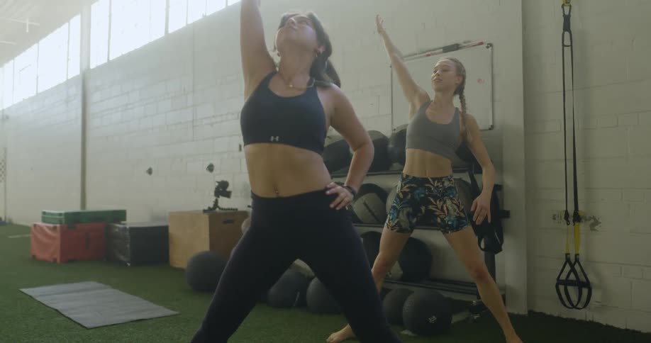 Two women are exercising in a gym during the day