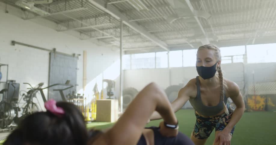 Two women in a room stretching with exercise equipment in the background