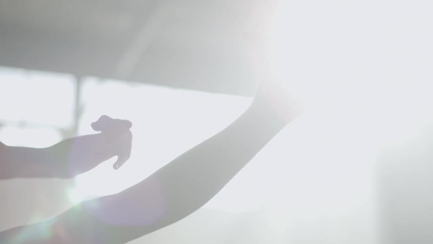 A woman performs graceful dance maneuvers in a building as sunlight shines through the windows