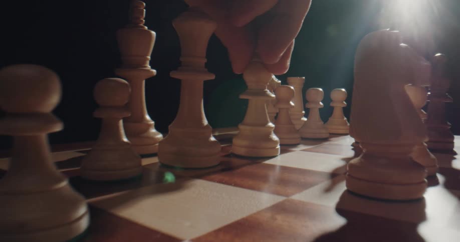 A chess player slides a piece on the board closer to him