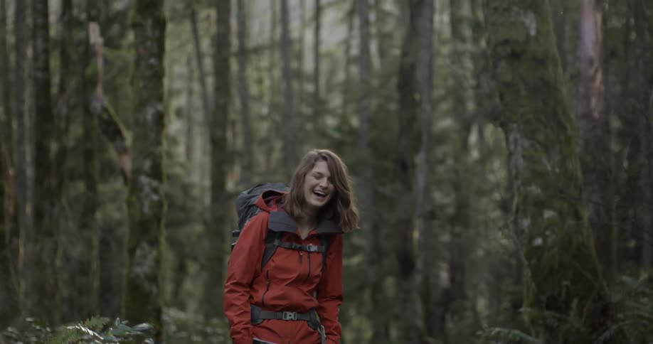 A woman is laughing as she stands in the woods