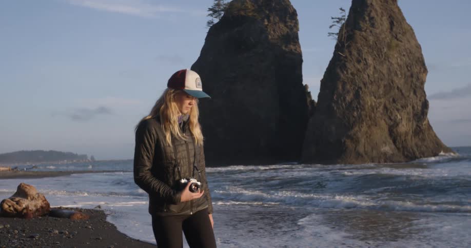 A woman walks on a beach with a camera hanging from her neck