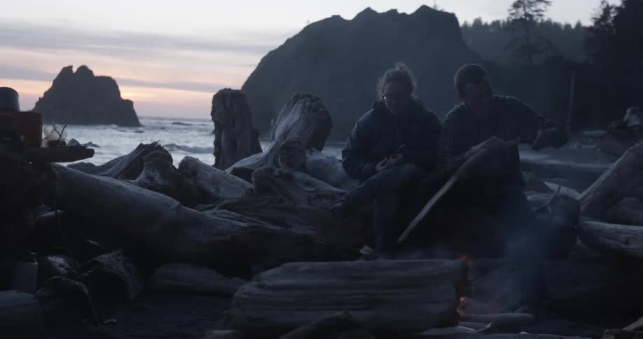 A couple sitting before a campfire on a coastline