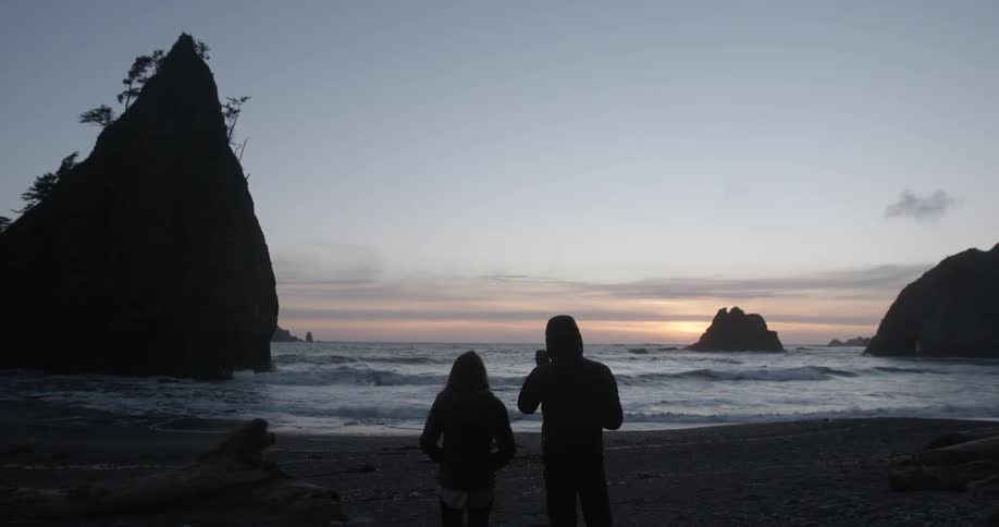 Two people stand by the shore at dawn