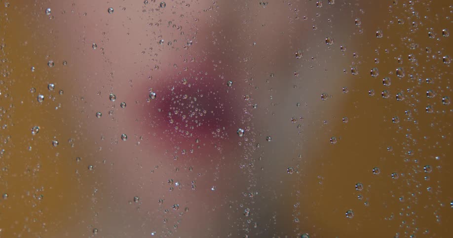 A woman smoking behind a piece of glass covered in water droplets