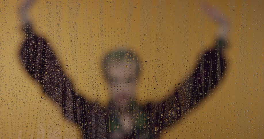 A woman is standing by a window when its raining