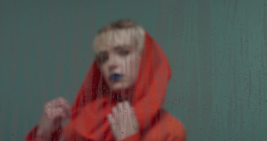 A woman is posing behind the wet glass