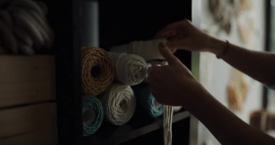 A woman picks up a roll of string twine for crafts from a shelf in the wall