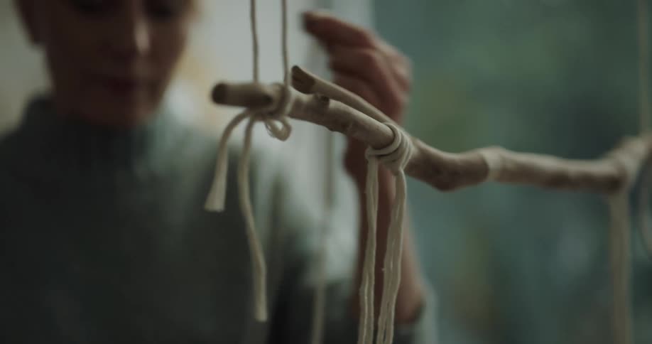 Woman braiding a white string around a hanging branch creating a hand made decoration